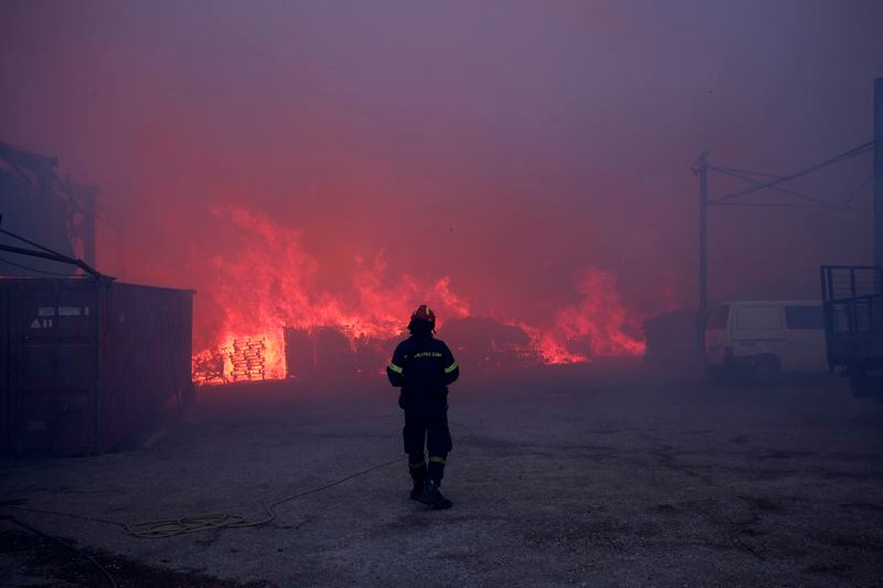 A firefighter stands in front of a burning business during a fire in northern Athens, Monday, Aug. 12, 2024, as hundreds of firefighters tackle a major wildfire raging out of control on fringes of Greek capital. (AP Photo/Aggelos Barai)