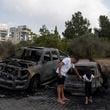 A man shows a burnt car to a girl, after a rocket launched from Lebanon, hit an area in Kfar Vradim, northern Israel, Monday, Oct. 7, 2024. (AP Photo/Leo Correa)