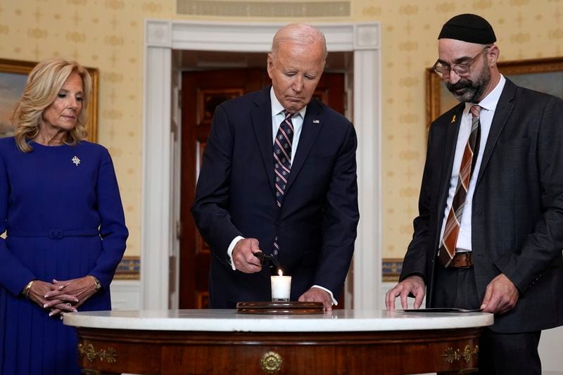 President Joe Biden, center, standing with first lady Jill Biden, left, and Rabbi Aaron Alexander of the Adas Israel Congregation, lights a memorial candle in the Blue Room of the White House in Washington, Monday, Oct. 7, 2024, to mark the one-year anniversary of the Hamas attack on Israel that left about 1,200 people dead. (AP Photo/Susan Walsh)