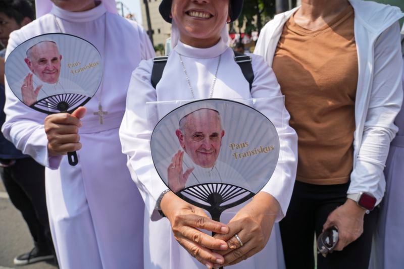 Devotees carrying hand fans printed with portraits of Pope Francis wait outside the Indonesian Bishops' Conference Headquarters to welcome the pope before his arrival for a meeting, in Jakarta, Indonesia, Thursday, Sept. 5, 2024. (AP Photo/ Tatan Syuflana)