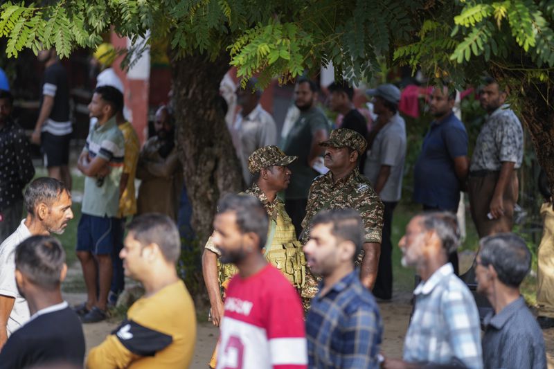 Paramilitary soldiers guard as people queue up to cast their vote at a polling booth during the final phase of an election to choose a local government in Indian-controlled Kashmir, in Jammu, India, Tuesday, Oct.1, 2024. (AP Photos/Channi Anand)