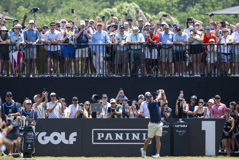 Captain Bryson DeChambeau, center right bottom, of Crushers GC, hits from the first tee as a gallery of fans look on during the final round of LIV Golf Nashville at The Grove, Sunday, June 23, 2024, in College Grove, Tenn. (Charles Laberge/LIV Golf via AP)