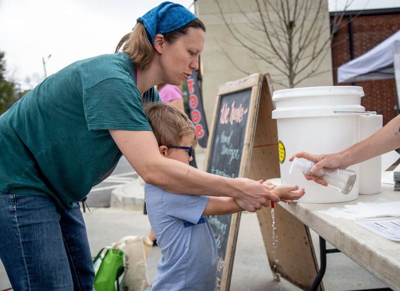 Amy Pearson helps her son Finn wash his hands before entering the Grant Park Farmers Market Sunday, March 29, 2020. STEVE SCHAEFER / SPECIAL TO THE AJC