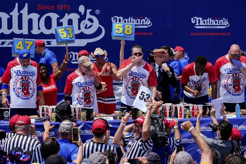 Patrick Bertoletti, center, competes in the men's division in Nathan's Famous Fourth of July hot dog eating contest, Thursday, July 4, 2024, at Coney Island in the Brooklyn borough of New York. Bertoletti ate 58 hot dogs. (AP Photo/Julia Nikhinson)