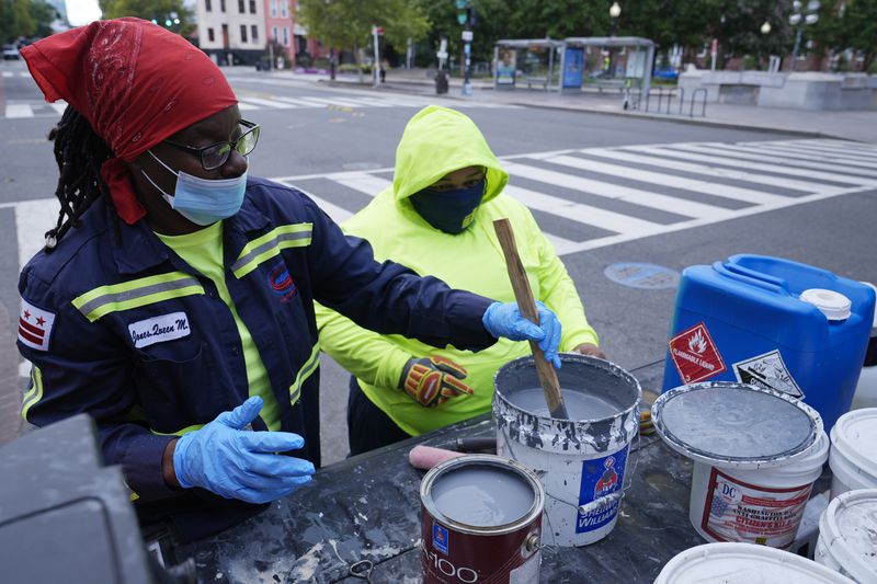 Queen Jones, left, stirs paint as Dominique Medley, right, watches, Tuesday, Aug. 20, 2024, as they prepare to remove graffiti in a neighborhood of Washington. (AP Photo/Susan Walsh)