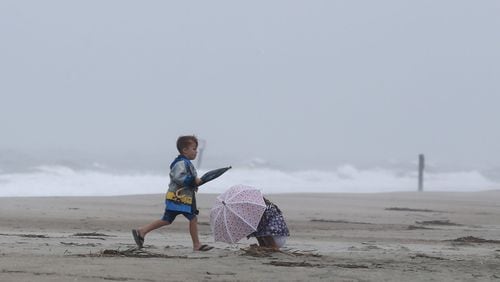 A young boy runs past his sister, who is huddled under an umbrella as the outer weather bands of Hurricane Idalia hit Tybee Island, Georgia on Wednesday, August 30, 2023. Chatham County was fortunate as Hurricane Idalia passed off shore, leaving only some downed trees behind.