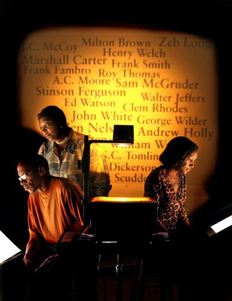 Members of the Afro-American Historical and Genealogical Society (left to right) Kenny Burton, Monica J. Hackney and Rhonda Barrow, pose for a photo as the known names of victims from the 1906 Atlanta race riots are projected onto a backdrop. The group was responsible for finding the only marked grave of a riot victim at South-View Cemetery.