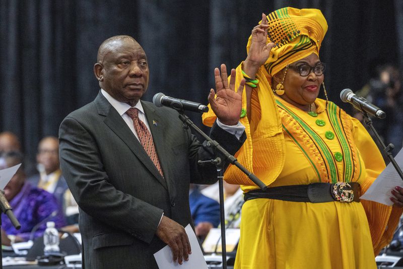 South African président Cyril Ramaphosa raises his hand as he is sworn is as a member of Parliament ahead of an expected vote by lawmakers to decide if he is reelected as leader of the country in Cape Town, South Africa, Friday, June 14, 2024. At right is Pemmy Majodina, an ANC lawmaker. (AP Photo/Jerome Delay)