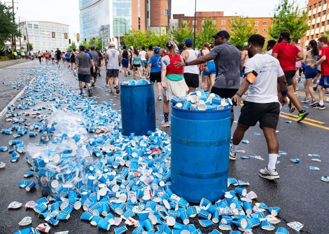 Runners toss empty cups towards over-full trash cans during the 55th running of The Atlanta Journal-Constitution Peachtree Road Race at "Cardiac Hill" on Peachtree Road NW in Atlanta on Thursday, July 4, 2024. (Seeger Gray / AJC)