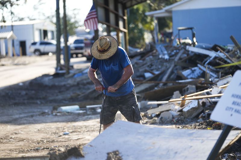 Chris Jordan, maintenance manager for Horseshoe Beach, tries to find a water shutoff valve amid the rubble of the destroyed city hall in the aftermath of Hurricane Helene, in Horseshoe Beach, Fla., Sunday, Sept. 29, 2024. (AP Photo/Gerald Herbert)