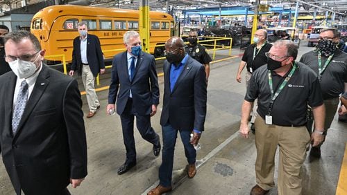 Blue Bird officials talk with Sen. Rev. Raphael Warnock (center right), during a tour of manufacturing facility at Blue Bird in 2021. The U.S. Department of Energy announced Thursday that it is giving Blue Bird $80 million to convert an old factory to making electric buses. (Hyosub Shin / Hyosub.Shin@ajc.com)