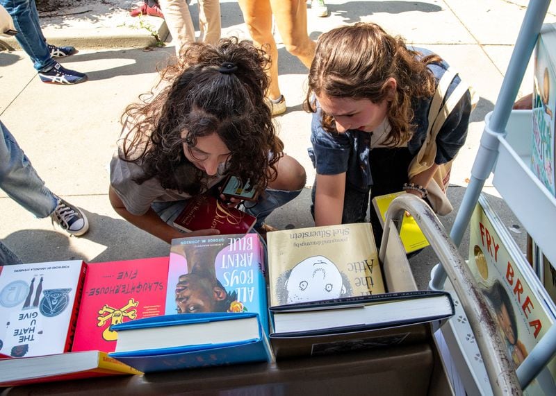 MoveOn Political Action's Banned Bookmobile is distributing free banned books at the kickoff of National Banned Book Week where Shereen Mendelson, left, and Isabella Lipham, of Sandy Springs, take a look at a few of the banned books that cannot be checked out at public school libraries Sunday, Oct 1, 2023 at Little Shop of Stories in Decatur Square.  (Jenni Girtman for The Atlanta Journal-Constitution)