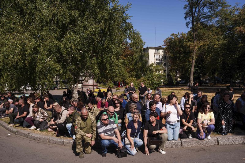 People kneel during the funeral ceremony of six Ukrainian servicemen killed in a Russian rocket attack at a Ukrainian military academy, in Poltava, Ukraine, Saturday Sept. 7, 2024. (AP Photo/Evgeniy Maloletka)