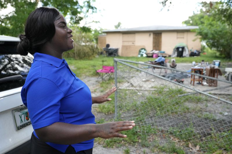 Erica Dorsett, program director of the TaskForce Fore Ending Homelessness, speaks with homeless people near an abandoned home on the first day of a statute that took effect, making it illegal in Florida to sleep on sidewalks, in parks, on beaches or in other public spaces — one of the country's strictest anti-homelessness laws, Tuesday, Oct. 1, 2024, in Fort Lauderdale, Fla. (AP Photo/Lynne Sladky)