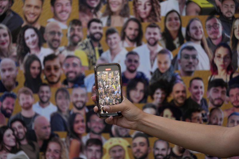 A woman takes photos at a mural with portraits of the victims at the site of the Nova music festival, where hundreds of revelers were killed and abducted by Hamas and taken into Gaza, on the one-year anniversary of the attack, near Kibbutz Reim, southern Israel, Monday, Oct. 7, 2024. (AP Photo/Ariel Schalit)