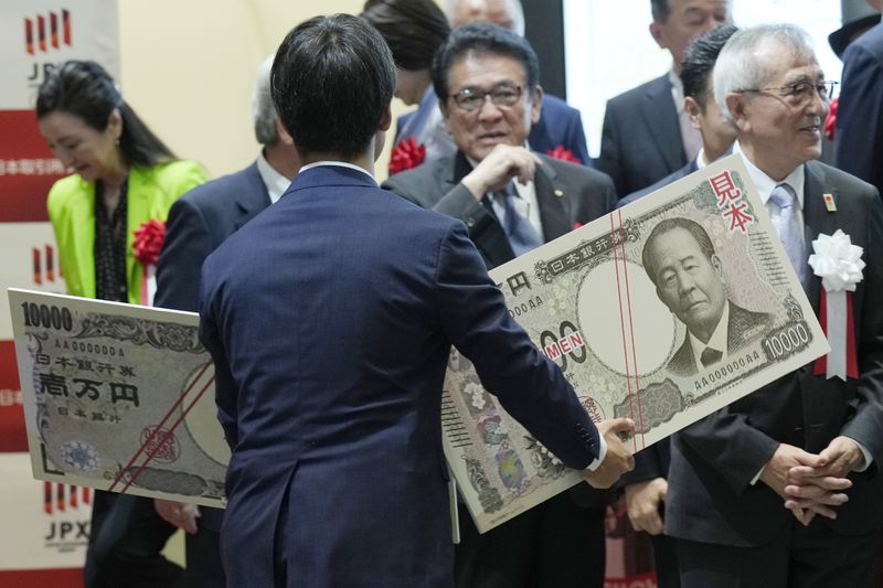 A staff holds an enlarged copies of the new and old 10000 yen banknotes after the "10,000 Yen Bill Handover Ceremony" at Tokyo Stock Exchange Wednesday, July 3, 2024, in Tokyo. Newly designed banknotes, 10,000 yen (about US$61), 5,000 yen (about US$30) and 1,000 yen (about US$6) went into circulation Wednesday for the first time in 20 years. (AP Photo/Eugene Hoshiko)