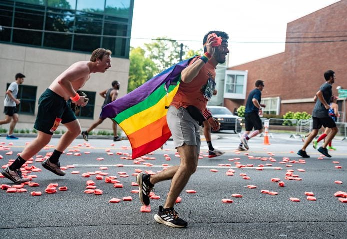A runner wearing a pride flag picks up a wristband thrown by Shepherd Center staff and patients during the 55th running of The Atlanta Journal-Constitution Peachtree Road Race at "Cardiac Hill" on Peachtree Road NW in Atlanta on Thursday, July 4, 2024. (Seeger Gray / AJC)