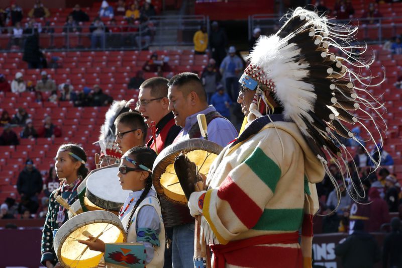 FILE - Members of the Blackfeet Nation perform as part of the Washington football team's observance of Native American Heritage Month prior to an NFL football game on Nov. 24, 2019, in Landover, Md. Many Native Americans thought a bitter debate over the U.S. capital’s football mascot was over when the team became the Washington Commanders. The original logo was designed by a member of the Blackfeet Nation. Now a white Republican U.S. senator from Montana is reviving the debate by blocking a bill funding the revitalization of the team's stadium unless the NFL and the Commanders bring back the former logo in some form. (AP Photo/Alex Brandon, File)