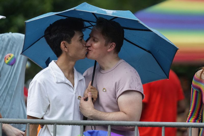 FILE - Jon Batayola, left, and Daniel Biginton embrace under an umbrella as they await the beginning of Chicago's annual Pride Parade, June 25, 2023, in Chicago. (AP Photo/Erin Hooley, file)