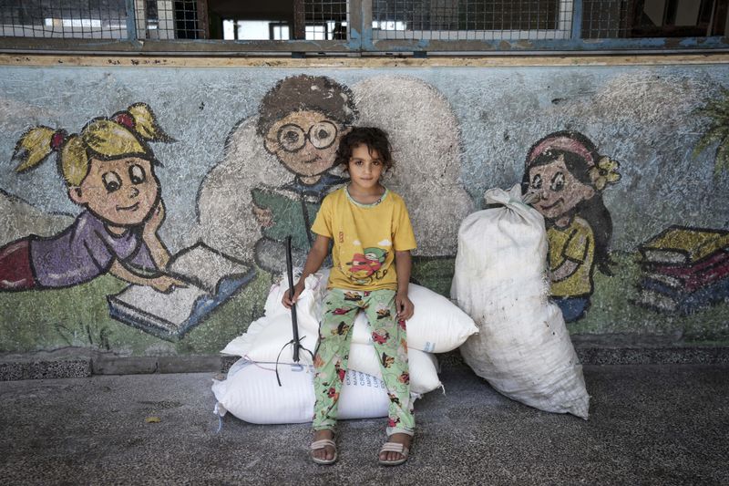 A Palestinian girl waits to evacuate a school that had been her shelter, in eastern Deir al-Balah, Gaza Strip, Friday, Aug. 16, 2024, after the Israeli military dropped leaflets asking civilians to evacuate from the area, saying forces plan to respond to rocket fire that targeted Israel. (AP Photo/Abdel Kareem Hana)