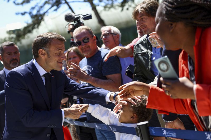 French President Emmanuel Macron greets a child after voting for the European election, Sunday, June 9, 2024 in Le Touquet-Paris-Plage, northern France. Polling stations opened across Europe on Sunday as voters from 20 countries cast ballots in elections that are expected to shift the European Union's parliament to the right and could reshape the future direction of the world's biggest trading bloc. (Hannah McKay/Pool via AP)