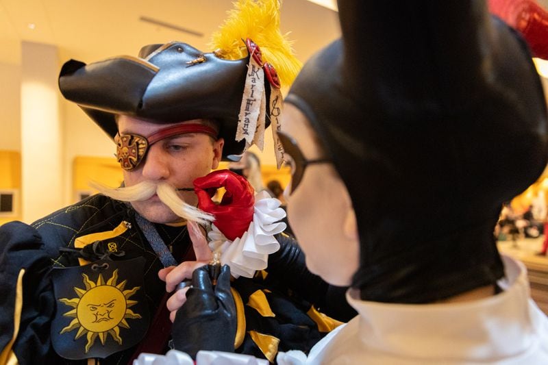 Nicole Pitts, cosplaying as Harley Quinn, helps her husband James, cosplaying as a Warhammer character, secure his fake mustache during Dragon Con in downtown Atlanta on Friday, August 30, 2024. (Arvin Temkar / AJC)