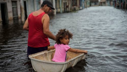 FILE - Jesus Hernandez guides his granddaughter Angelina via a container through a street flooded in the passing of Hurricane Helene, in Batabano, Mayabeque province, Cuba, Sept. 26, 2024. (AP Photo/Ramon Espinosa, File)