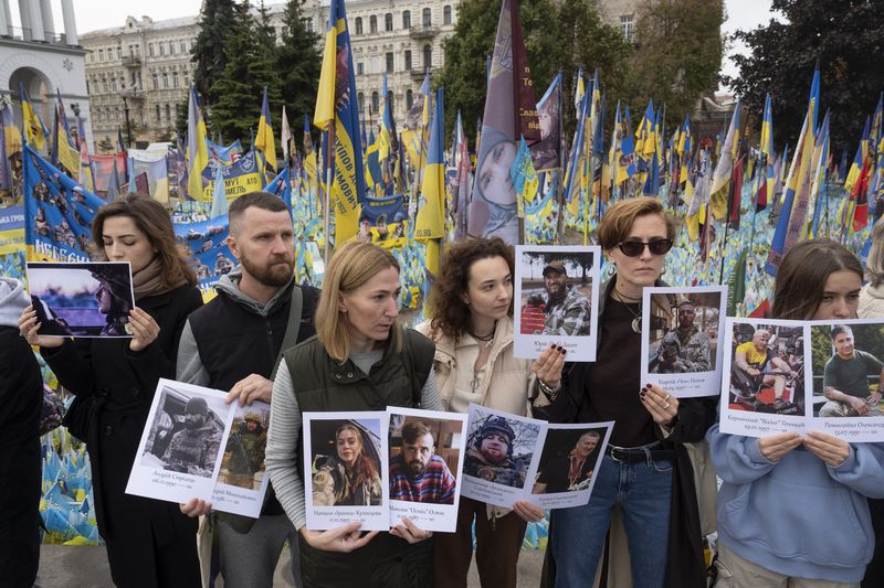 People hold photos of their relatives soldiers to keep a nationwide minute of silence in memory of fallen soldiers, who defended their homeland in war with Russia, on Defenders Day at the improvised war memorial in Independence square in Kyiv, Ukraine, Tuesday, Oct. 1, 2024. (AP Photo/Efrem Lukatsky)