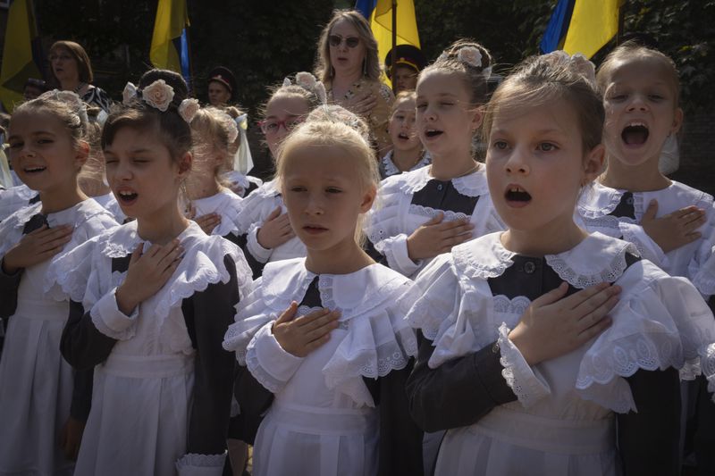 Schoolgirls sing the national anthem on the first day at school in a cadet lyceum in Kyiv, Ukraine, Monday, Sept. 2, 2024. Children and students went to school despite the fact that Kyiv was hit by massive Russian missile barrage early in the morning, causing fires, damaged buildings and infrastructure objects. (AP Photo/Efrem Lukatsky)