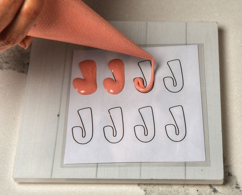 If desired when making royal icing transfers, draw your design, like these tiny candy canes, on paper, then place the paper under a plastic sheet. When dry, the transfers can be lifted from the plastic sheet and applied to cookies. (Styling by Sam Opdenbosch / Chris Hunt for the AJC)