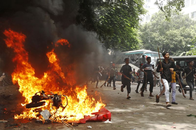 FILE - Men run past a vehicle at the Bangabandhu Sheikh Mujib Medical University Hospital that was set on fire by protesters during a rally against Prime Minister Sheikh Hasina and her government, in Dhaka, Bangladesh, on Aug. 4, 2024. (AP Photo/Rajib Dhar, File)