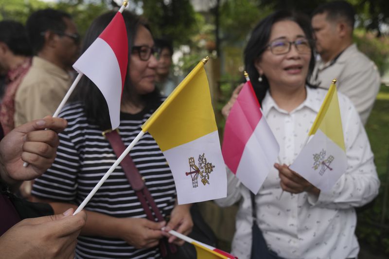 People hold Indonesian and Vatican flags as they welcome the arrival of Pope Francis outside the Vatican Embassy in Jakarta, Indonesia, Tuesday, Sept. 3, 2024. (AP Photo/Dita Alangkara)