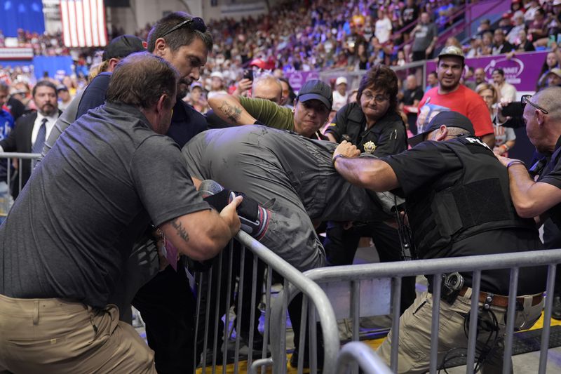 Police remove a man, center, who had climbed onto the media riser, as Republican presidential nominee former President Donald Trump speaks at a campaign event, Friday, Aug. 30, 2024, in Johnstown, Pa. (AP Photo/Alex Brandon)