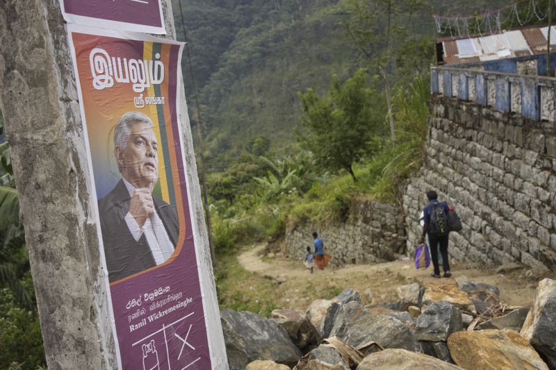 Tea plantation workers at Spring Valley Estate walk past an election poster with a portrait of the Sri Lankan president Ranil Wickremesinghe, ahead of the country's presidential election, in Badulla, Sri Lanka, Monday, Sept. 9, 2024. (AP Photo/Eranga Jayawardena)