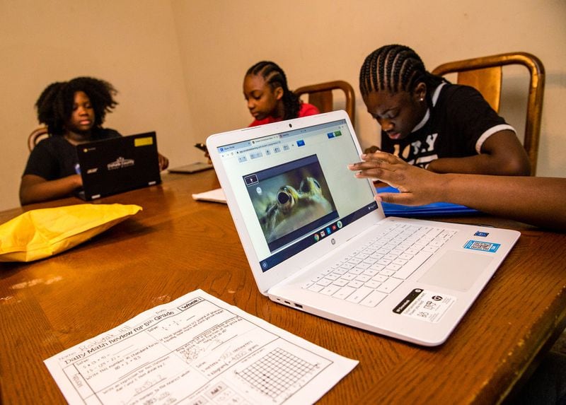 Rakiyah Hill, 10, front right, a 5th grader at McClendon Elementary, learns cell structure on a computer her mother had to buy this month so all children would be able to get their school work done. Raina Hill, 12, back left, a 6th grader at Champion Middle School uses the only DeKalb County computer they have, while Rihanna Hill,13, in red, an 8th grader at Champion Middle School uses a tablet to do school work and sister, Roniyah Hill, black shirt braids,15, a 10th grader at Martin Luther King High School uses her phone to look up definitions.(Jenni Girtman for Atlanta Journal Constitution)