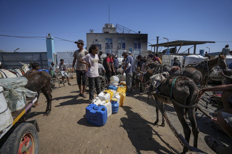 Displaced Palestinians line up to collect water, in Deir al Balah, central Gaza Strip, Friday, Aug. 23, 2024. (AP Photo/Abdel Kareem Hana)