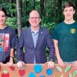 Faustina Barcena (left) stands with Adam Pomeranz, president and CEO of Annandale Village (center), and her brother, John, in front of a bench she created for the Suwanee assisted living facility. Courtesy