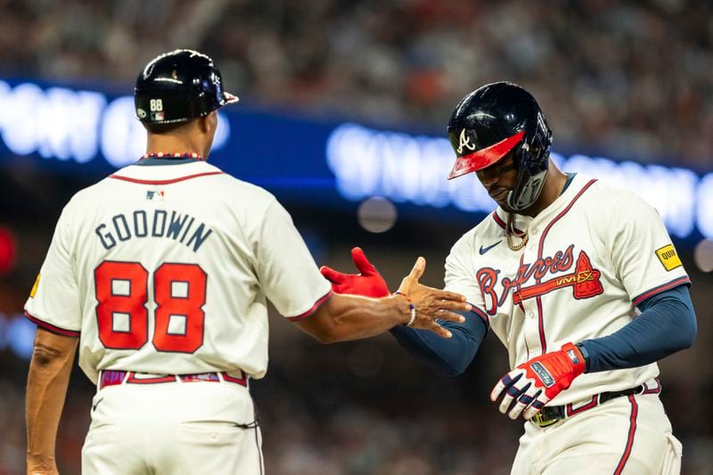 Atlanta Braves' Jorge Soler, right, high fives first base coach Tom Goodwin, left, after hitting a single in the fifth inning of a baseball game against the New York Mets, Tuesday, Sept. 24, 2024, in Atlanta. (AP Photo/Jason Allen)