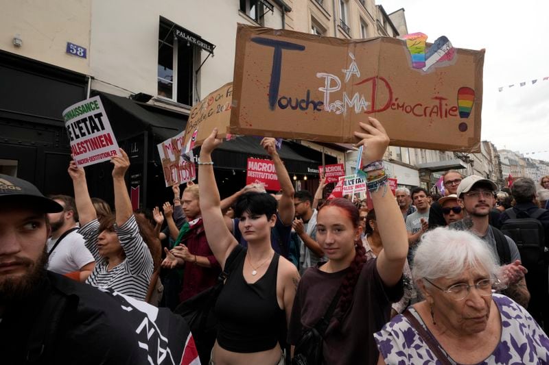 A demonstrator, on right, holds a placard which reads 'don't touch my democracy' during a protest, responding to a call from the far-left party who criticized as a power grab the president's appointment of a conservative new prime minister, Michel Barnier, in Paris, France, Saturday, Sept. 7, 2024. (AP Photo/Michel Euler)