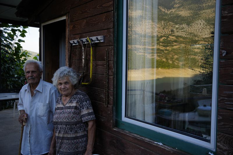 Constantinos Gerodimos, left, 90-year-old farmer who used to live in the village of Kallio before it was submerged in the artificial Mornos lake, and his wife Maria pose, some 200 kilometers (125 miles) northwest from Athens, central Greece, on Thursday, Sept. 5, 2024. (AP Photo/Thanassis Stavrakis)