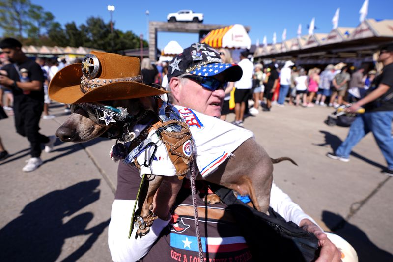 Bob Ankrum holds his service dog, Buttercup, who has a toy pistol fastened on to her shoulder, as they attend the State Fair of Texas in Dallas, on Friday, Sept. 27, 2024. (AP Photo/Tony Gutierrez)