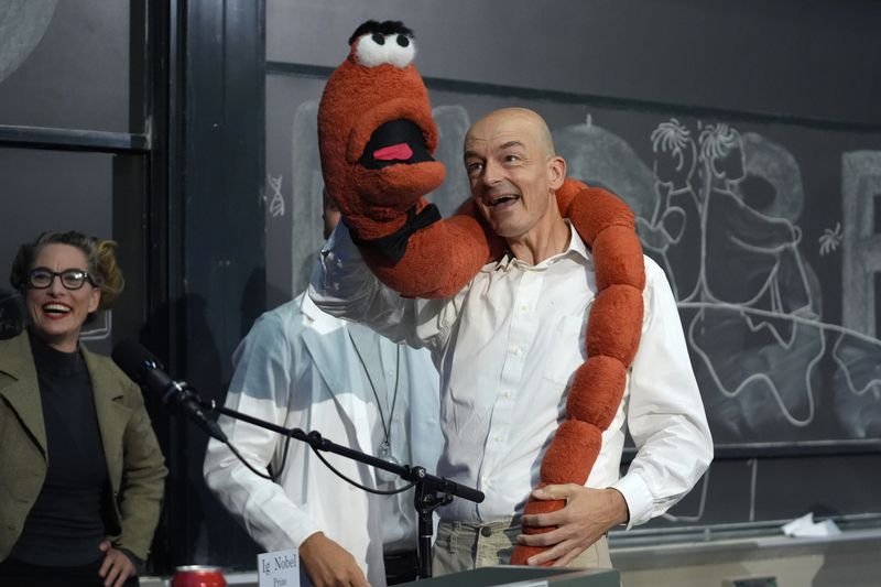 Professor Sander Woutersen, right, displays an oversized stuffed worm while accepting a shared Ig Nobel Prize in chemistry for working with a team of researchers using chromatography to separate drunk and sober worms, during a performance, Thursday, Sept. 12, 2024, at the Ig Nobel Prize ceremony at Massachusetts Institute of Technology, in Cambridge, Mass. (AP Photo/Steven Senne)