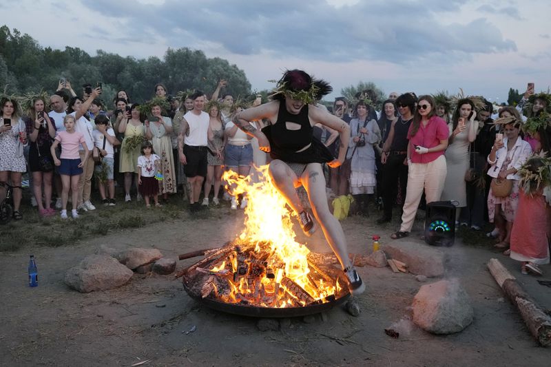 A Ukrainian woman jumps over fire during a traditional Ukrainian celebration of Kupala Night, in Warsaw, Poland, on Saturday, June 22, 2024. Ukrainians in Warsaw jumped over a bonfire and floated braids to honor the vital powers of water and fire on the Vistula River bank Saturday night, as they celebrated their solstice tradition of Ivan Kupalo Night away from war-torn home. (AP Photo/Czarek Sokolowski)