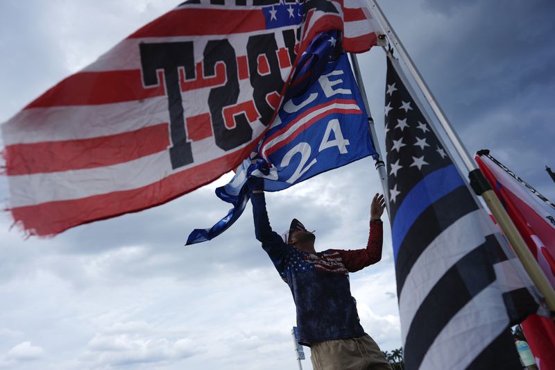 Jestin Nevarez, of Lake Worth, Fla., adjusts flags flying from his car as he shows support for Republican presidential nominee and former President Donald Trump outside of Trump's Mar-a-Lago estate, a day after an apparent assassination attempt, in Palm Beach, Fla., Monday, Sept. 16, 2024. (AP Photo/Rebecca Blackwell)