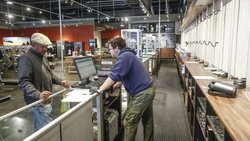 Grahame Grantham (center), a manager at Stoddard’s Range and Guns in Atlanta, in front of an empty display wall, helps a customer wanting to make a purchase. The store has seen an uptick in ammunition and gun sales as the coronavirus threat intensifies. Bob Andres / robert.andres@ajc.com