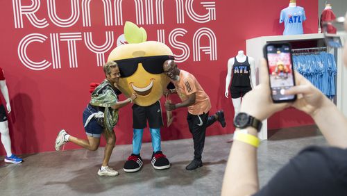 Martiel Kirksey-Parker, left, and McKinley Parker, pose for a photo with Pete The Peach after picking up their bibs for the Atlanta Journal-Constitution Peachtree Road Race at the Peachtree Health and Fitness Expo in Atlanta on Tuesday, July 2, 2024.   (Ben Gray / Ben@BenGray.com)
