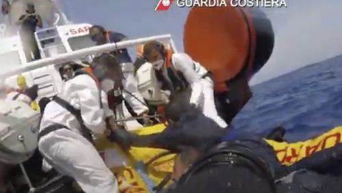 The image made from a video provided by the Italian coast guard shows a patrol boat rescuing migrants from a sinking ship off the coast of Lampedusa, Italy. (Italian Coast Guard via AP)