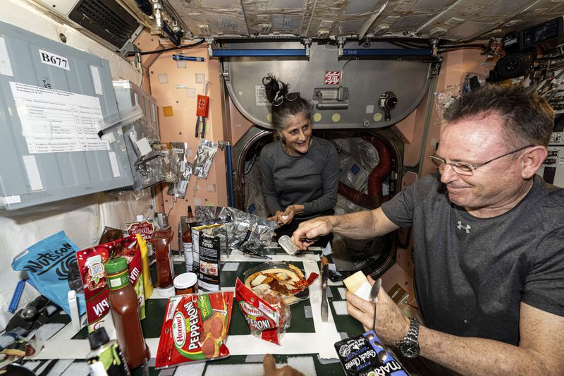 In this image released by NASA, NASA astronauts Suni Williams and Butch Wilmore, both Expedition 71 Flight Engineers, make pizza aboard the International Space Station's galley located inside the Unity module on Sept. 9, 2024. Items are attached to the galley using tape and velcro to keep them from flying away in the microgravity environment. (NASA via AP)