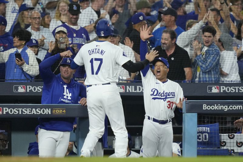 Los Angeles Dodgers' Shohei Ohtani (17) celebrates with manager Dave Roberts, middle right, after Ohtani scored on a single by Teoscar Hernández during the fourth inning in Game 1 of baseball's NL Division Series against the San Diego Padres, Saturday, Oct. 5, 2024, in Los Angeles. (AP Photo/Mark J. Terrill)