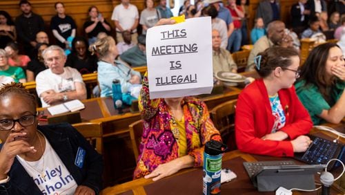 An attendee holds a sign that says “This Meeting is Illegal” during a hastily planned State Election Board meeting July 12 at the Georgia Capitol in Atlanta. (Arvin Temkar / AJC)